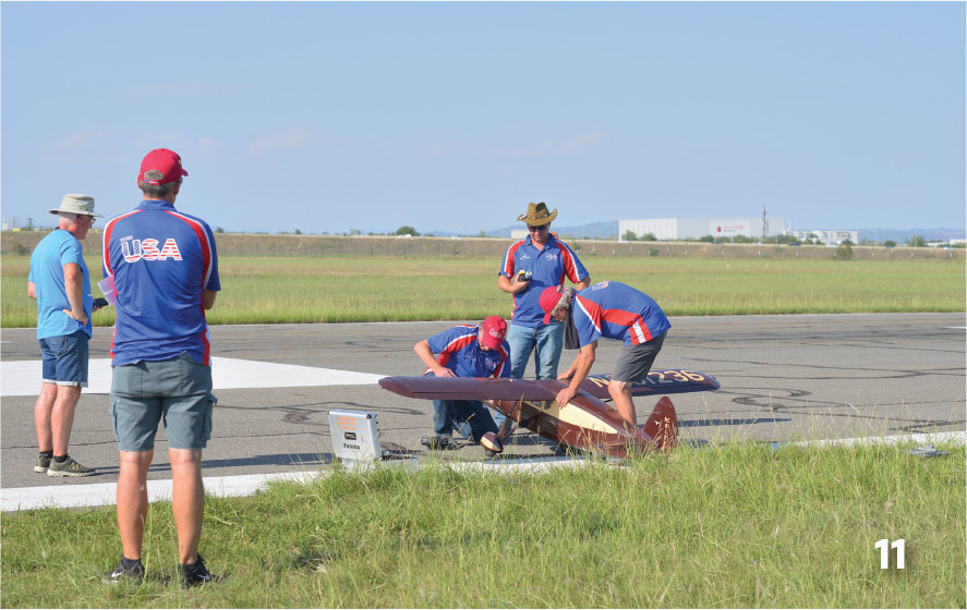Team in red, white, and blue shirts prepare a model plane on a runway.