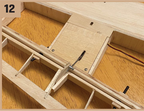 Wooden model airplane assembly step 12, showing fuselage and wing connection.