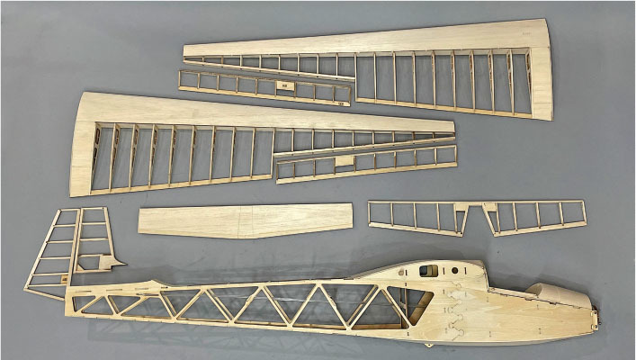 Wooden model airplane parts laid out on a gray surface.