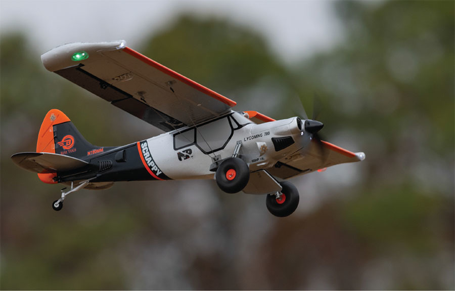 RC airplane with orange and black accents flying outdoors.