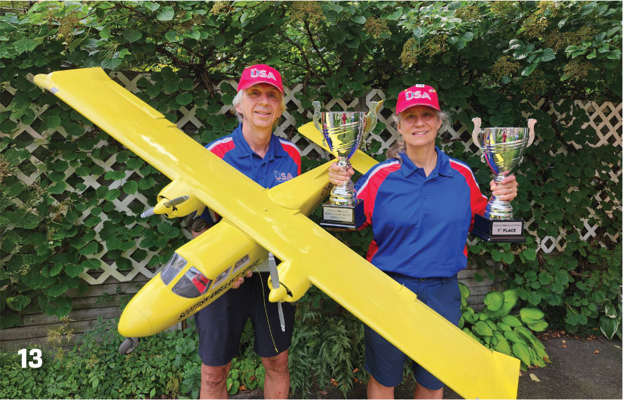 Two people holding trophies and a large yellow model plane, wearing USA hats.