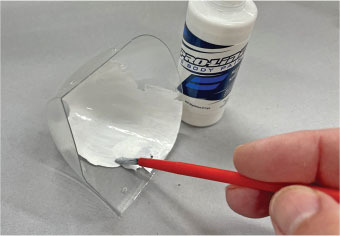 Hand painting clear plastic with white paint, paint bottle nearby.