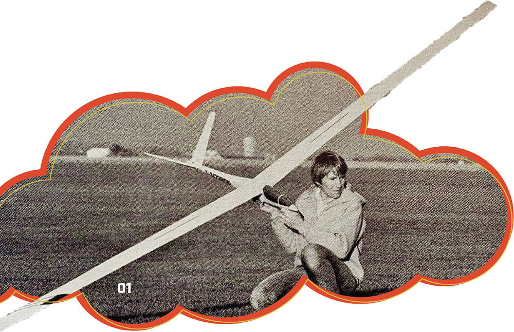 Man crouched on grass, holding a model glider.