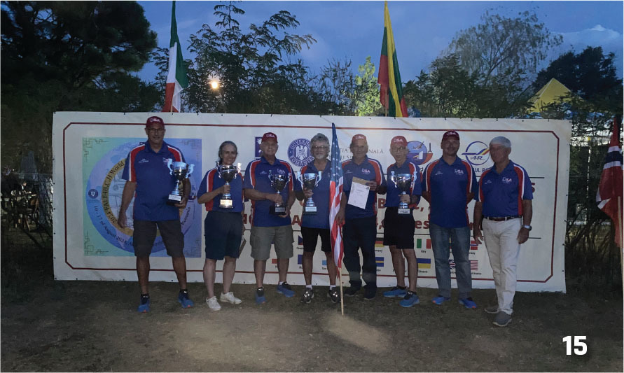 Group of people holding trophies, standing in front of a banner with flags.
