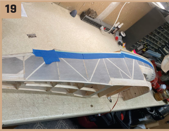 Model airplane wing under construction on a workbench, labeled "19."