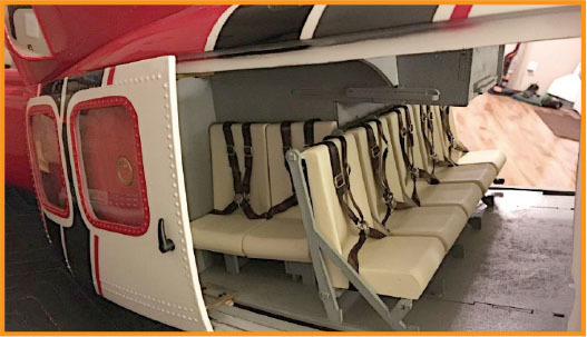 Interior of a red and white helicopter, with beige seats and harnesses.