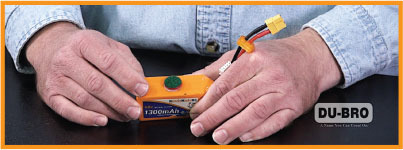 Hands holding an orange 1300mAh battery, DU-BRO logo in corner.