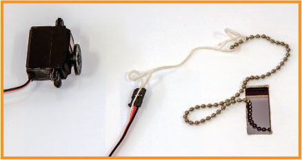 A motor with wires, a string, and a beaded chain on a white surface.