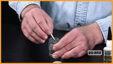 Hands stirring liquid in a small jar next to Du-Bro adhesive bottle.