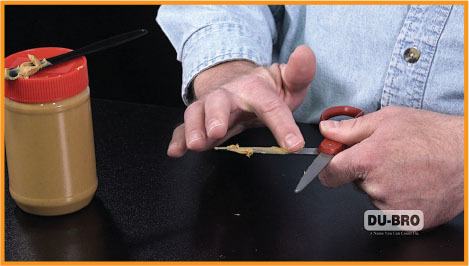 Man scraping peanut butter off finger with scissors, jar on table.