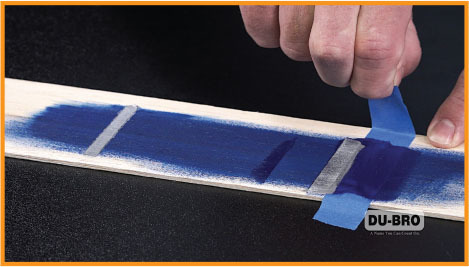 Hand peeling blue tape from a painted wood strip, DU-BRO logo visible.