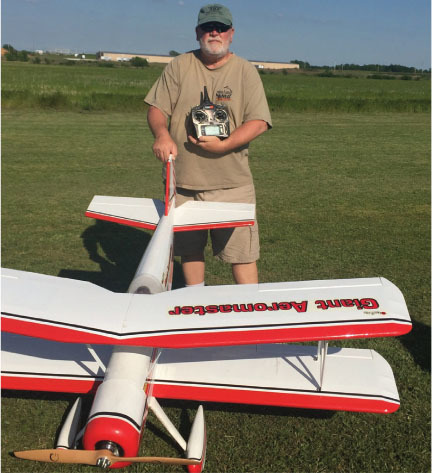 Man holding a remote next to a large model airplane on grass.