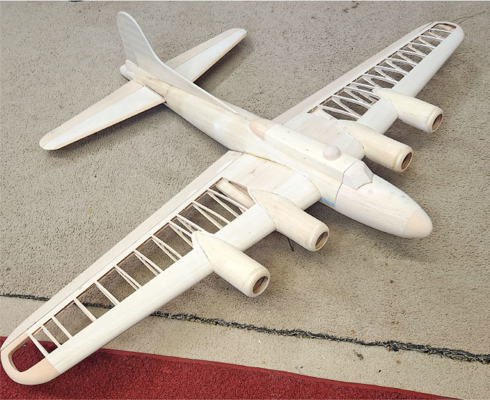 Wooden model airplane with exposed framework on carpet.