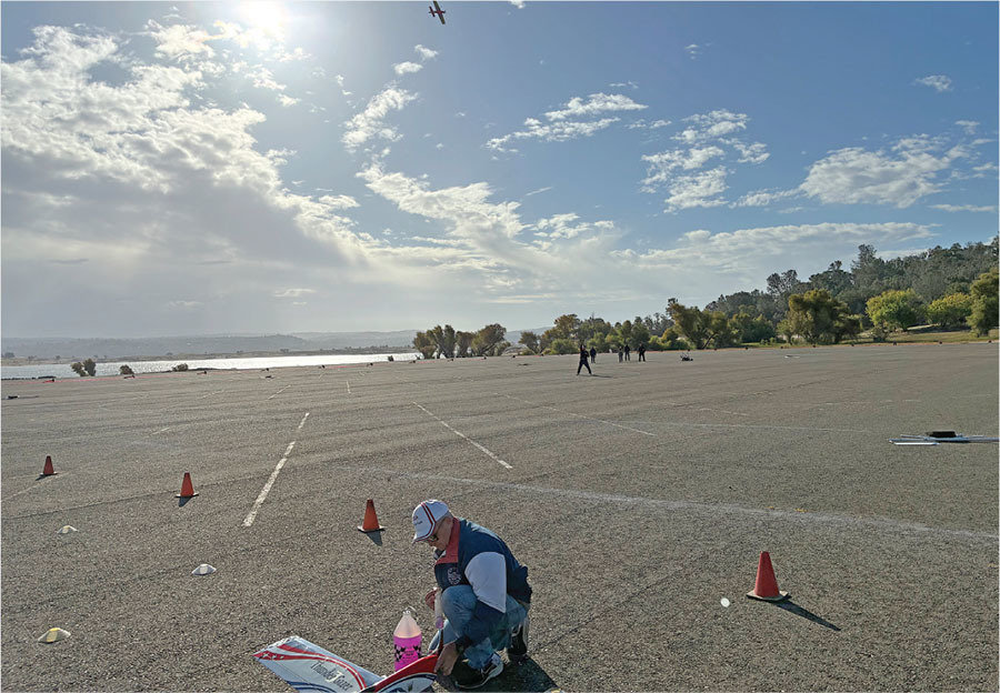 Man assembling a model airplane on an empty lot under a sunny sky.
