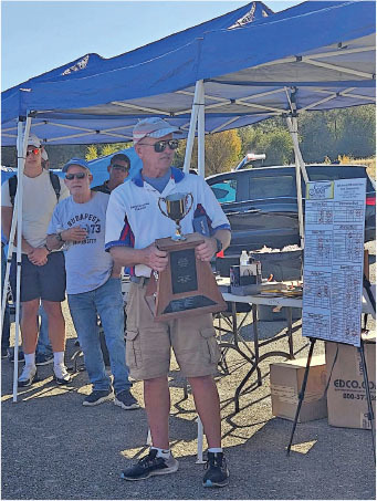 Man holding trophy under blue tent, people and table behind him.