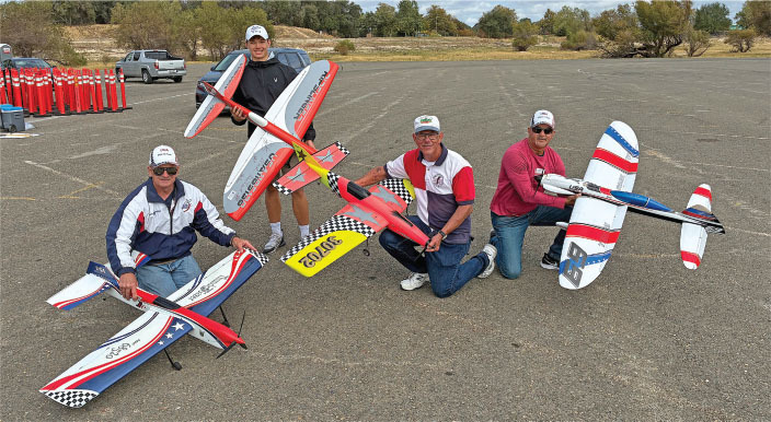 Four men holding colorful remote-controlled model airplanes in a parking lot.