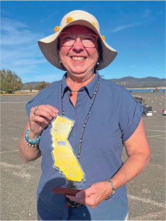Smiling woman holding yellow award, wearing sun hat, outdoors.