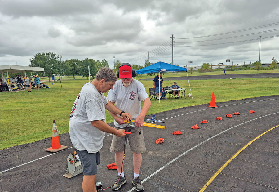 Two men in casual clothing work on a model airplane on a track.