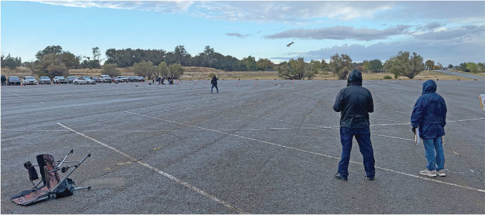 People flying kites in a large open parking lot with cloudy skies.