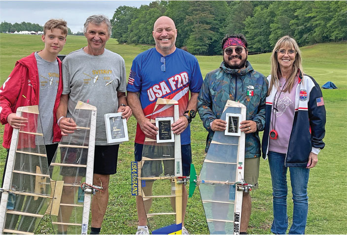 Five people standing outdoors, holding model planes and plaques, smiling.