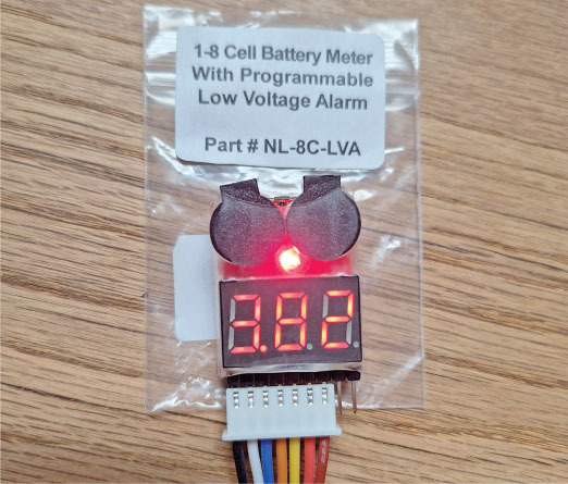 Battery meter with red LED display reading "3.82" on a wooden table.