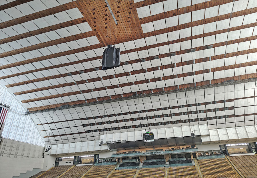 Stadium ceiling with wood beams and lights, scoreboard, and seating below.