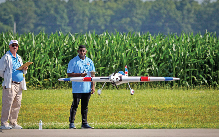 Two men with a model plane near a cornfield runway.