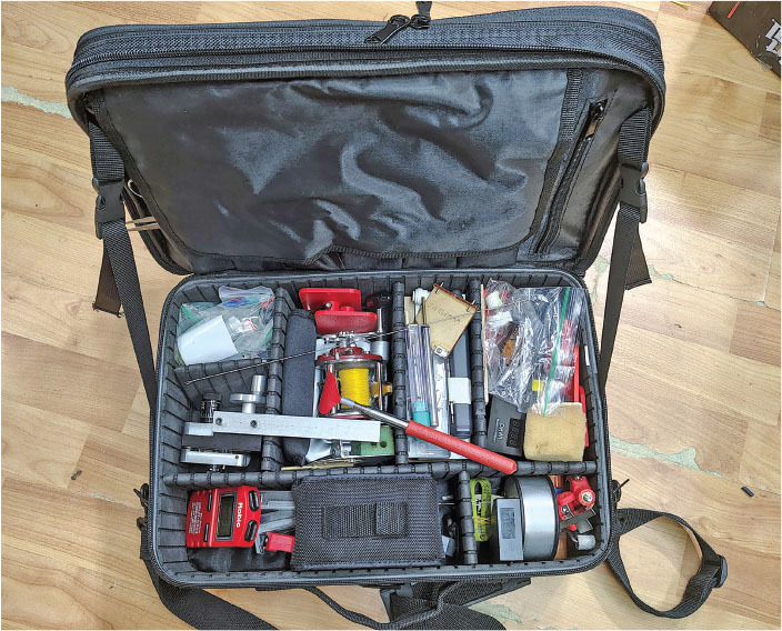 Open toolbox with various tools and supplies on a wooden floor.