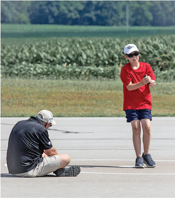 Man sitting on pavement, boy in red shirt standing nearby on a sunny day.
