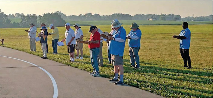 People standing in a line on grassy field, reading from clipboards.