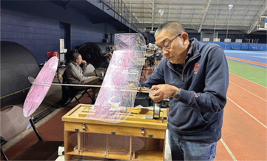 Man adjusting a model glider in an indoor sports arena.