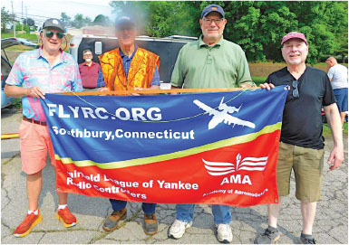 Four men hold a FLYRC.ORG banner promoting Fairfield League of Yankee Radio Controllers.