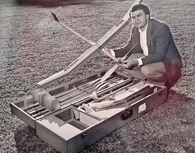 Man in suit kneeling on grass with open model aircraft kit.