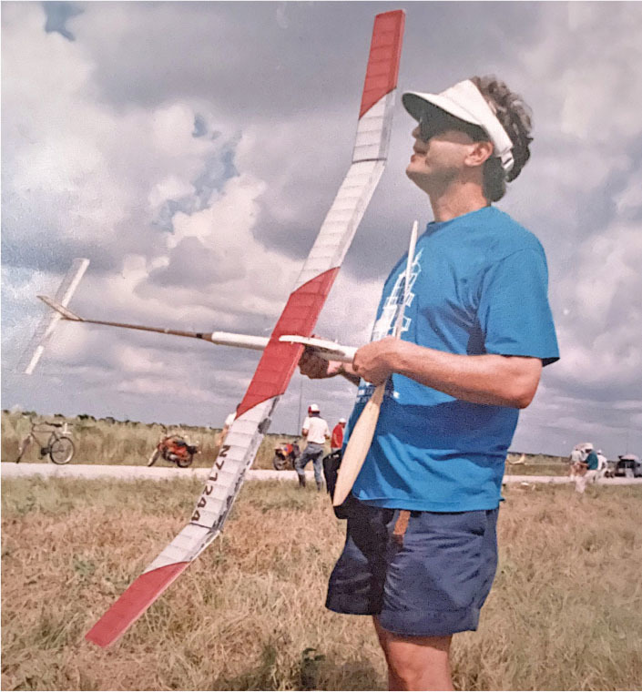 Man holding a large model airplane outdoors, wearing a blue shirt and visor.