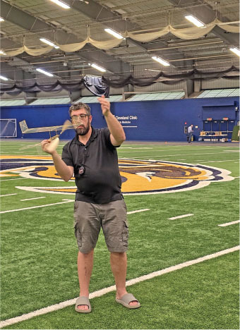 Man flying a model airplane indoors on a sports field.