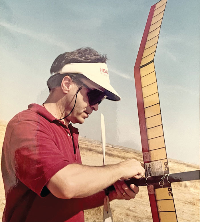 Man in red shirt adjusts model airplane outdoors.
