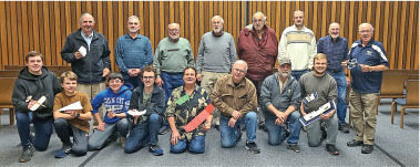 A group of men posing in a room, some holding model airplanes.