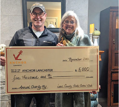 Two people smiling, holding a large $5,000 check for Anchor Lancaster.