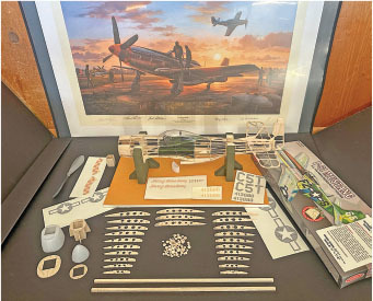 Model airplane kit pieces with a framed painting of planes at sunset.