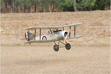Model biplane flying low over a grassy field.