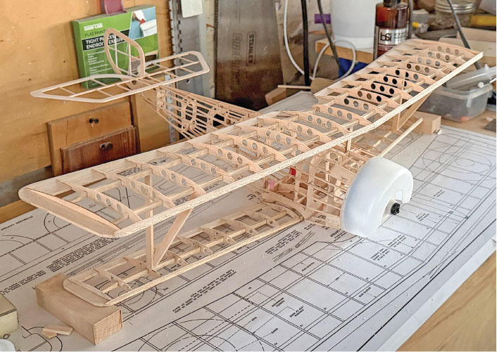Wooden model airplane in progress on a workbench with plans underneath.