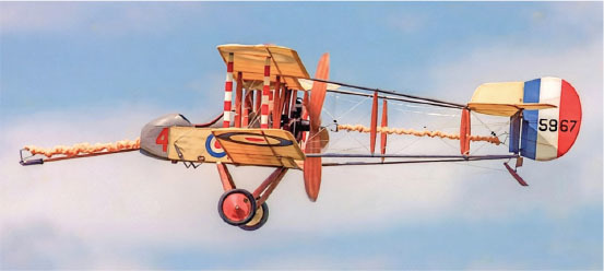 Vintage biplane with colorful tail markings flying in a blue sky.