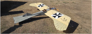 Replica of a vintage biplane with yellow wings on grassy ground.