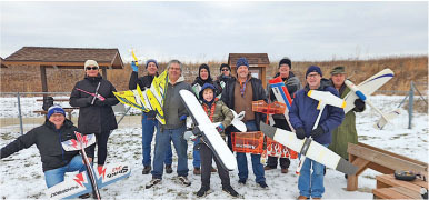 Group holding model airplanes outside on a snowy day.