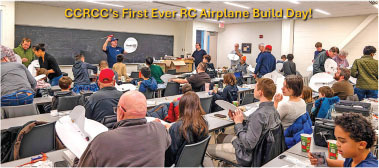 People in a classroom building RC airplanes, with a banner above.