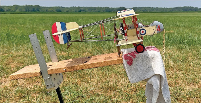 Model biplane on a wooden stand, outdoors on grass.