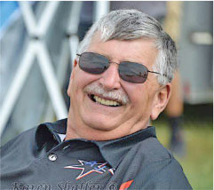 Smiling man in sunglasses and black shirt outdoors.