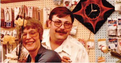 Smiling couple in a store aisle with a black and red wall clock.