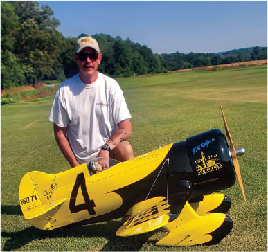 Man kneeling on grass with a large yellow and black model plane.