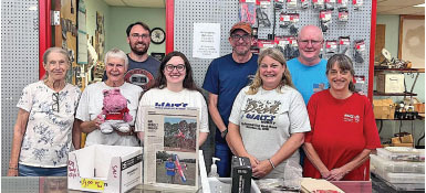 Group of nine smiling people standing in a store with merchandise in the background.